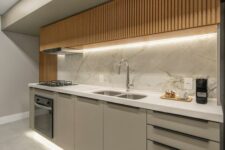 a minimalist kitchen with plain greige lower and stained fluted upper cabinets, lights, a white backsplash and countertops