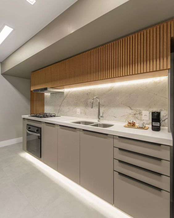 a minimalist kitchen with plain greige lower and stained fluted upper cabinets, lights, a white backsplash and countertops