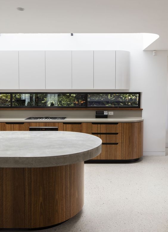 a minimalist kitchen with stained and sleek white curved cabinets, a window backsplash and a curved kitchen island with a stone countertop