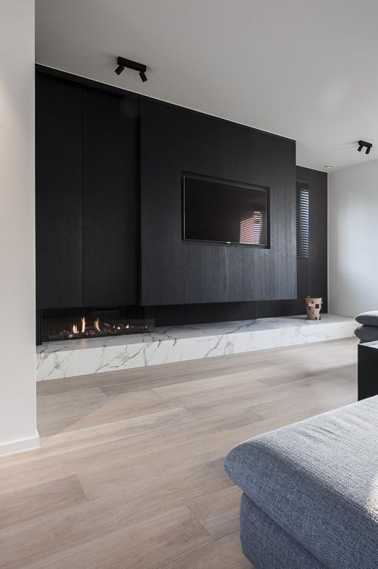 a minimalist living room with a black wood wall, a small built-in fireplace, a white marble slab, chic furniture