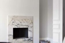a minimalist living room with a built-in fireplace surrounded with white marble, a white sofa, a dark coffee table
