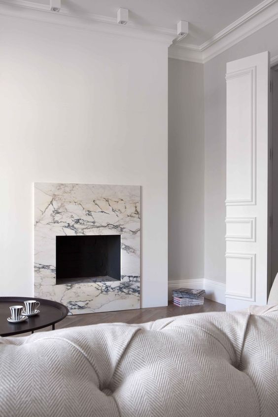 a minimalist living room with a built-in fireplace surrounded with white marble, a white sofa, a dark coffee table