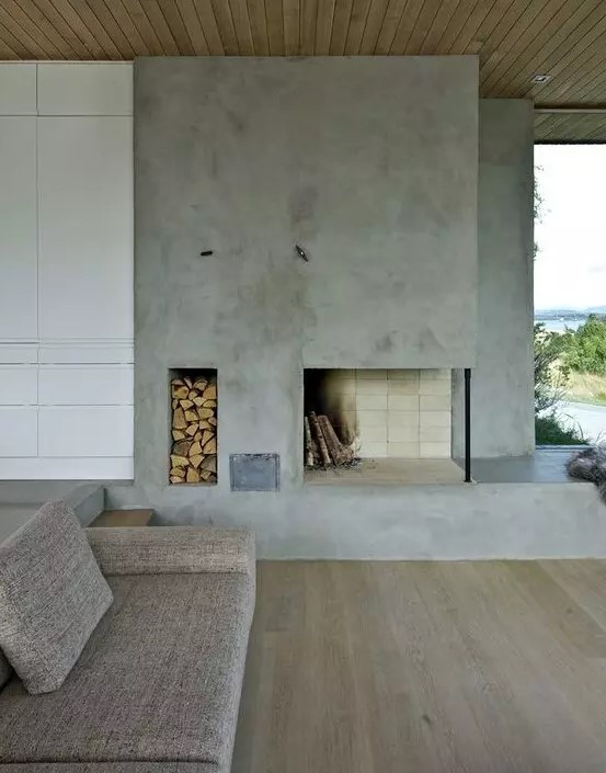 a minimalist living room with a concrete fireplace, a niche for firewood storage and simple furniture