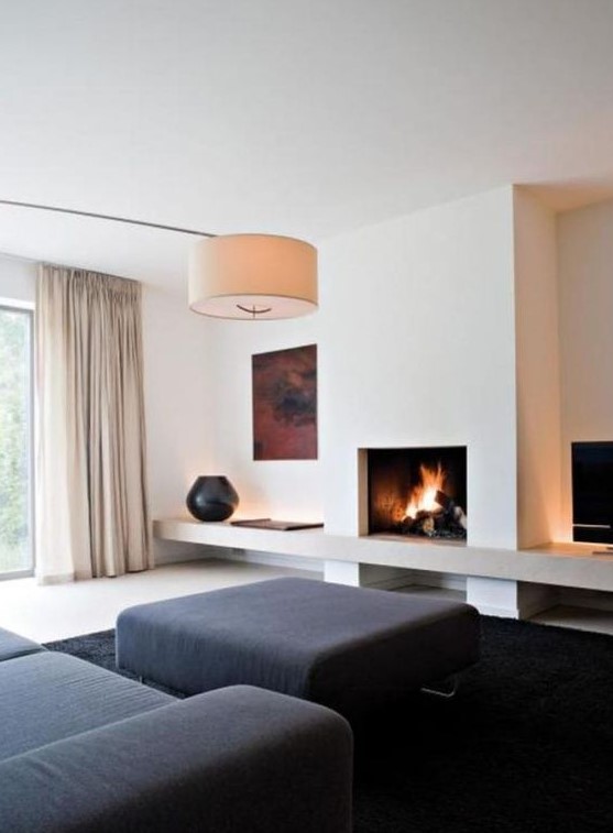a minimalist living room with black furniture and a rug, a fireplace, an artwork, a lamp and neutral curtains