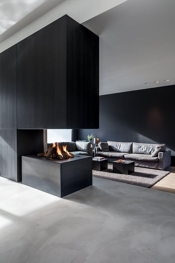 a minimalist space with a black accent wall, an ethanol fireplace under a large panel, a grey sofa, black tables