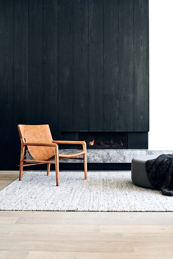 a minimalist space with a built-in fireplace, a black wood cover over it, a grey marble slab, a leather chair, a grey pouf