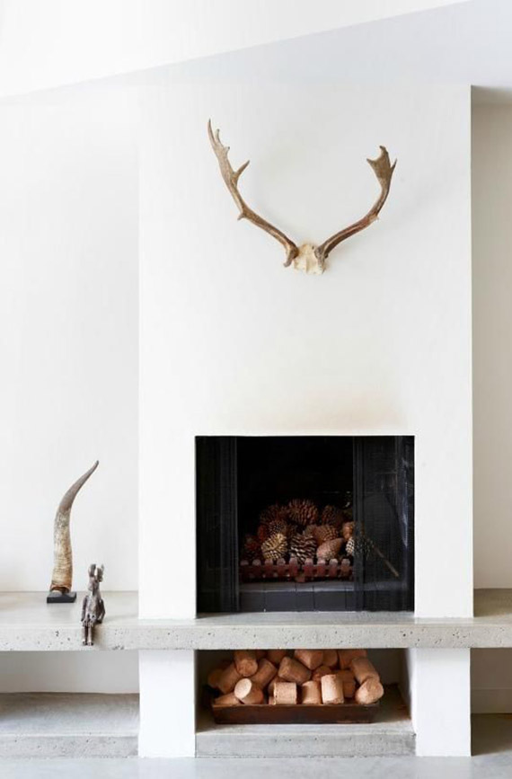 a minimalist white fireplace with a tray with pinecones, antlers, horns and other decor