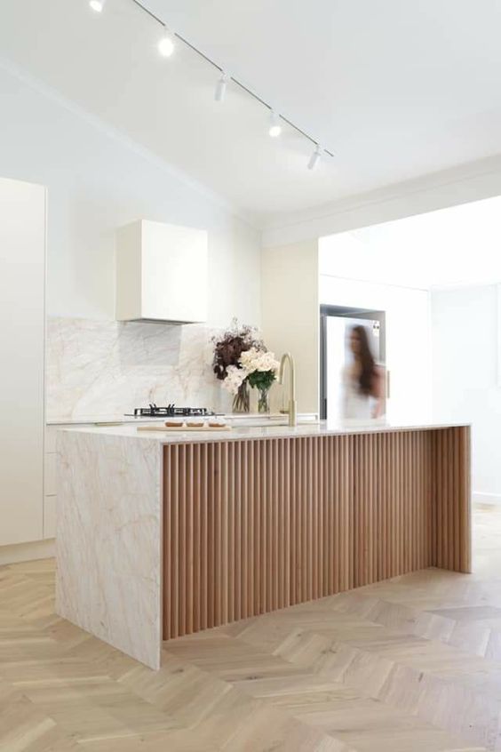 a minimalist white kitchen with a white stone backsplash and countertops and a ribbed kitchen island plus spotlights