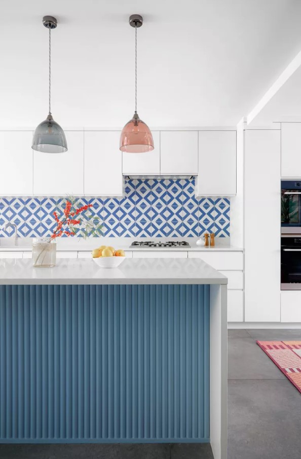 a minimalist white kitchen with sleek cabinets, a blue and white geometric tile backsplash, a blue fluted kitchen island with a white stone countertop