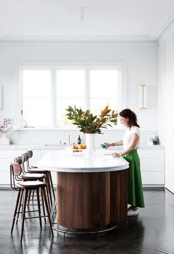 a minimalist white kitchen with sleek cabinets, a fluted curved kitchen island, tall stools and cool lamps