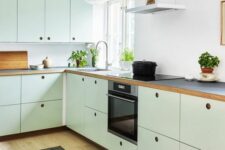 a mint green kitchen with plywood cabinets, a white backsplash, black countertops, no handles and built-in appliances
