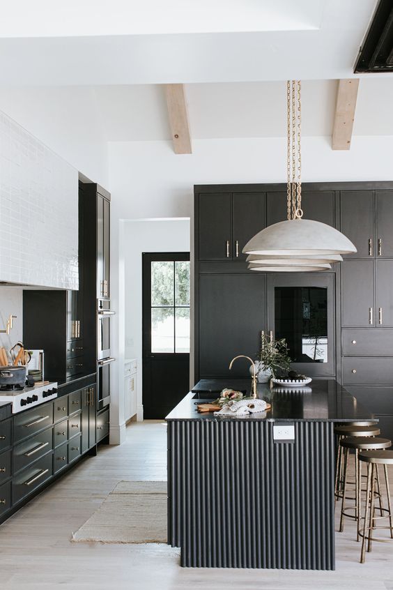 a modern black and white kitchen with black cabinetry, a white tile hood and a black fluted kitchen island with glossy countertops