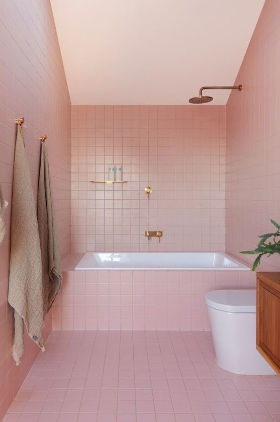 a modern glam bathroom clad with pink tiles and finished off with brass and gold fixtures for a chic look
