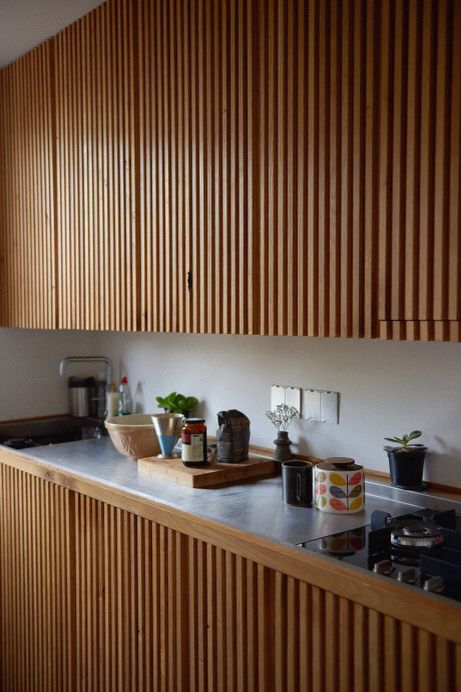 a modern kitchen done with stained ribbed cabinets with no handles, a neutral backsplash and countertop is a cool mid century modenr idea