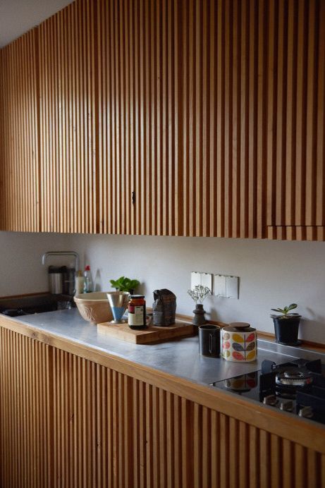a modern kitchen done with stained ribbed cabinets with no handles, a neutral backsplash and countertop is a cool mid-century modenr idea
