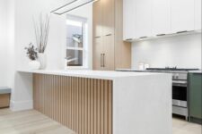 a modern kitchen with white and stained cabinets, built-in lights and a fluted kitchen island with a waterfall countertop