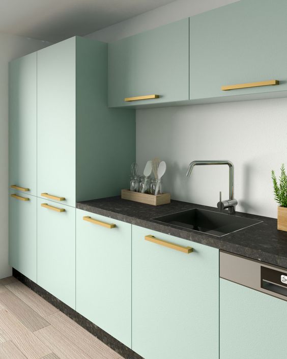 a modern mint green kitchen with a black countertop and a neutral backsplash plus some brass fixtures is super cool