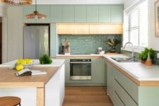 a modern pastel green kitchen with sleek cabinets, white stone countertops, a glossy green tile backsplash and woven pendant lamps