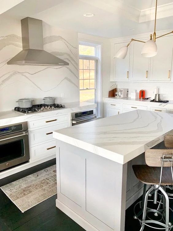 a modern white kitchen with shaker cabinets, a grey kitchen island, a white quratz backsplash and countertops plus a modern chandelier
