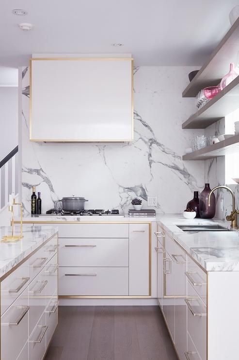 a modern white kitchen with sleek cabinets with gilded edges and a matching hood plus a white quartz backsplash and countertops