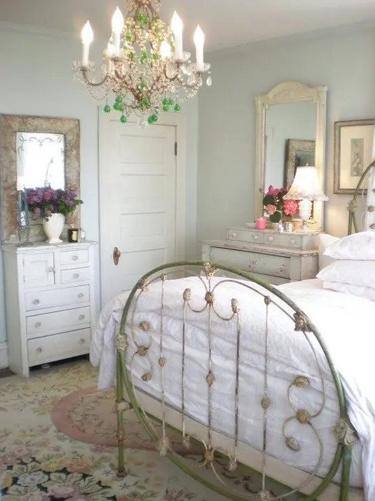 a neutral and pastel vintage bedroom with a metal bed, a crystal chandelier, mirrors and a chic floral rug