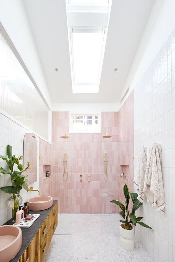 a neutral bathroom with a skylight, a pink accent wall, a floating vanity, pink sinks and potted plants