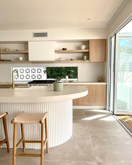 a neutral kitchen with stained cabinets, open shelves, a window backsplash and a ribbed curved kitchen island with a thick countertop