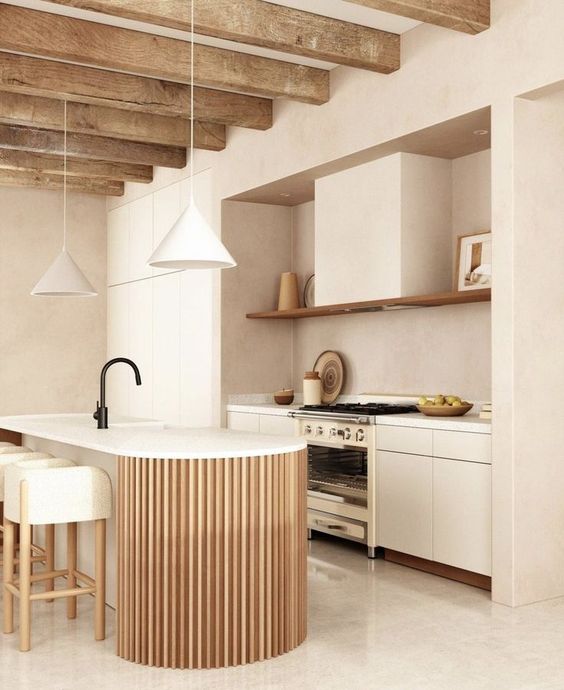 a neutral warm colored kitchen with sleek cabinets, an open shelf, a curved and fluted kitchen island and pendant lamps