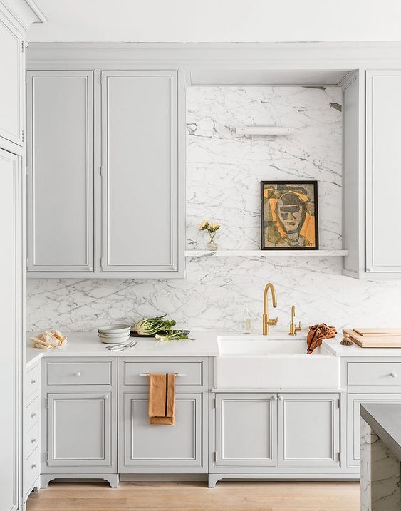 a pale grey kitchen with shaker cabinets, a white quartz backsplash and countertops, gold touches and lights