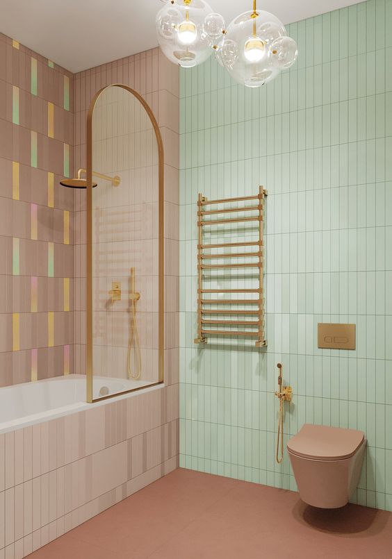 a pastel bathroom with a green and mauve skinny tile wall, a mauve floor and a toilet, brass fixtures