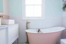 a pastel bathroom with blush and pastel blue walls, white square and pink hexagon tiles, a pink bathtub and a white vanity