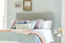 a pastel bedroom with a grey upholstered bed with pastel bedding, a mini gallery wall, a refined nightstand with blooms