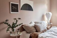a pastel bedroom with dusty pink walls, a bed with neutral bedding, a mini gallery wall, a nightstand with greenery