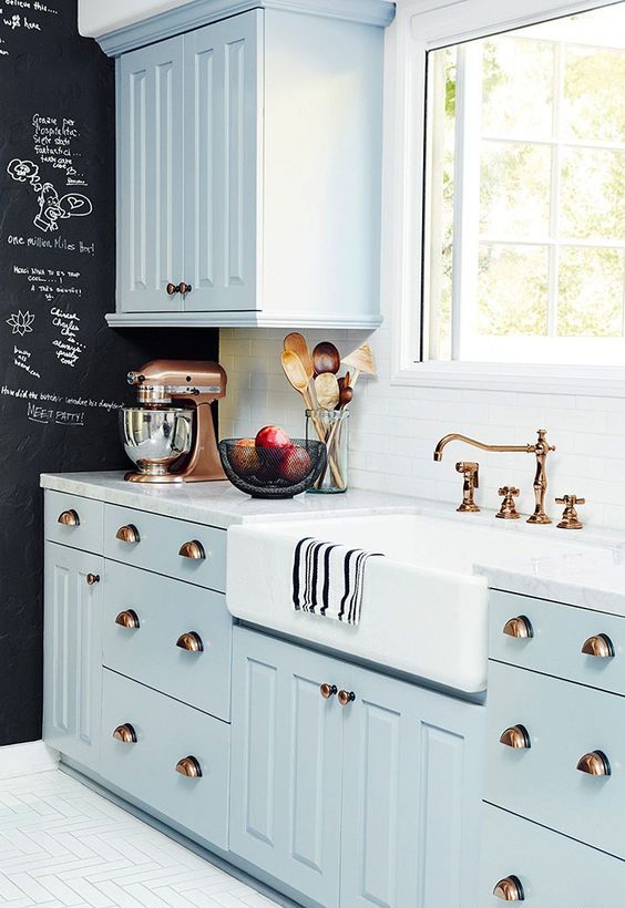 a pastel blue famrhouse kitchen with shaker cabinetry, a white stone countertop and a white tile backsplash plus a chalkboard wall