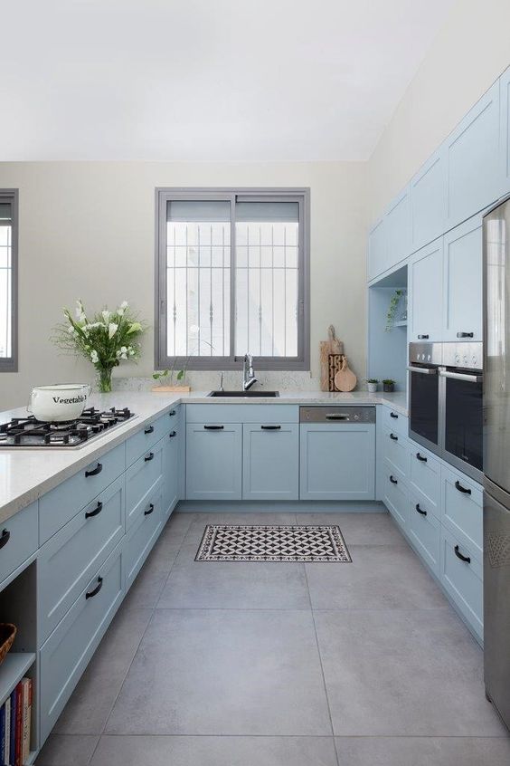 a pastel blue farmhouse kitchen with shaker cabinets, white stone countertops, black handles, built-in appliances