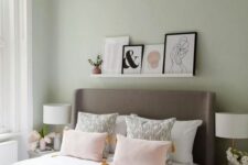 a pastel green bedroom with an upholstered bed, pink bedding, a ledge with artworks and a chandelier