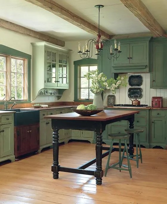 a pastel green vintage-inspired kitchen is made cozier with wooden beams and an antique dining table that acts as a kitchen island