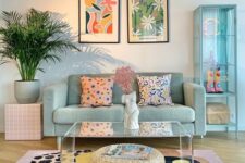 a pastel living room with a mint blue sofa, a mint blue glass cabinet, a pastel printed rug, a pink stool and printed pillows