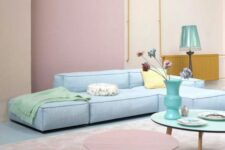 a pastel living room with blush walls, a pink accent, a pastel blue sofa, pastel side tables and a blue lamp
