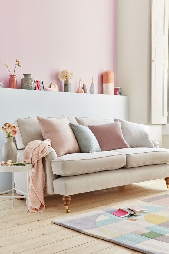 a pastel living room with neutral walls and a pink accent wall, refined furniture, pastel vases and pillows plus a color block rug