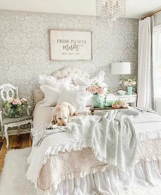 a pastel vintage bedroom with a printed wallpaper wall, a refined bed and nightstands, printed bedding and a crystal chandelier