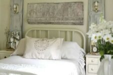 a pastel vintage bedroom with light green walls, a metal bed, neutral furniture, whitewashed decor and a fringe piece plus a crystal chandelier