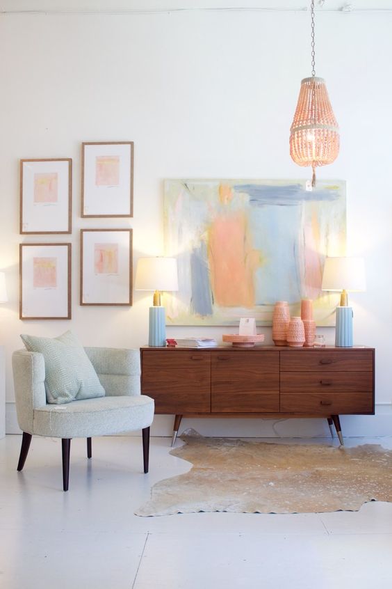 a pretty living room with a mint green chair, a stained credenza with an arrangement of pink vases and blue lamps, a pastel gallery wall