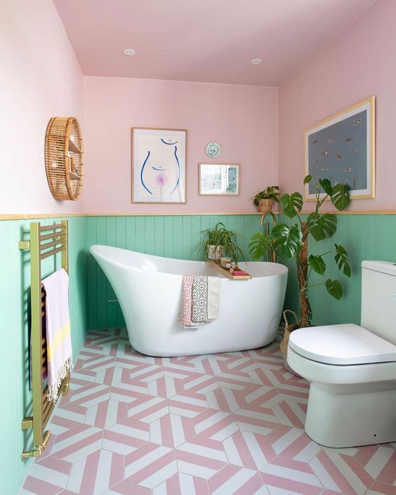 a pretty pastel bathroom with pink and green paneled walls, white appliances, gold touches and lovely artworks is fun