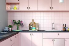a pretty pastel pink kitchen with leather handles, a matching pink backsplash and black countertops
