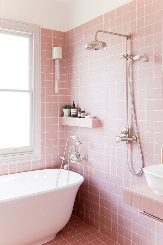 a pretty pink bathroom clad with square tiles, a white tub and a sink, a built-in shelf and a vanity plus lights