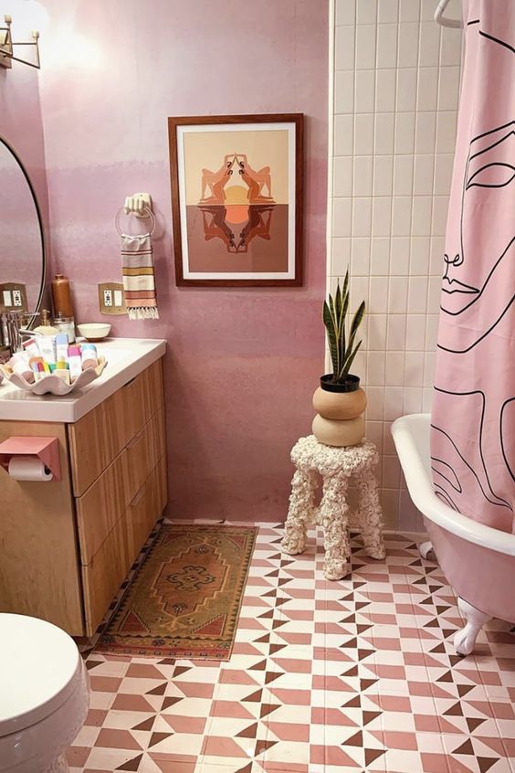 a quirky pink bathroom with geo tiles on the floor, a pink free-standing bathtub and a pink curtain, a light-stained vanity