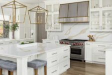 a refined creamy kitchen with shaker cabinets, a white quartz backsplash and countertops, oversized brass pendant lamps