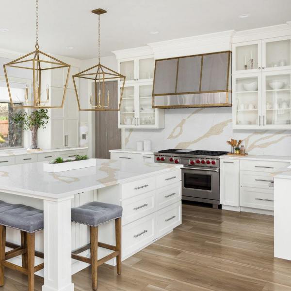 a refined creamy kitchen with shaker cabinets, a white quartz backsplash and countertops, oversized brass pendant lamps