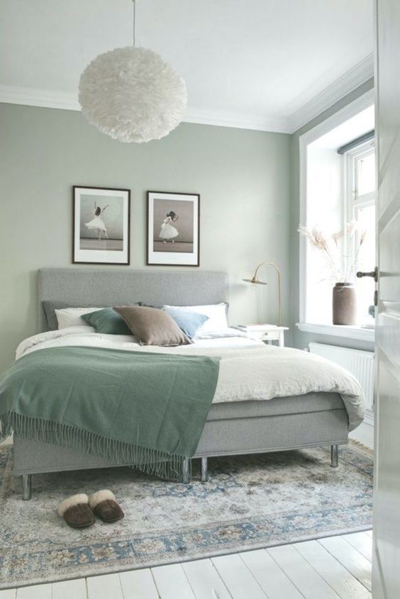 a sage green bedroom with a grey upholstered bed, pastel bedding, a printed rug and a couple of artwork